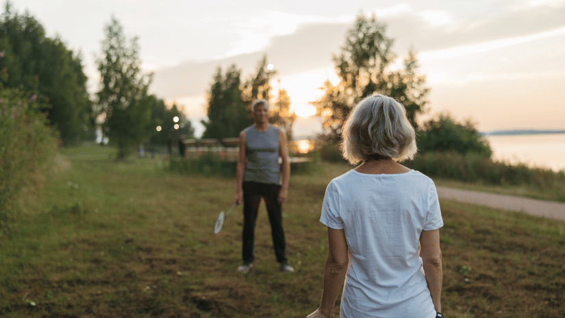 Several people playing frisbee on a grassy field near a lake at sunset, enjoying a recreational activity in nature
