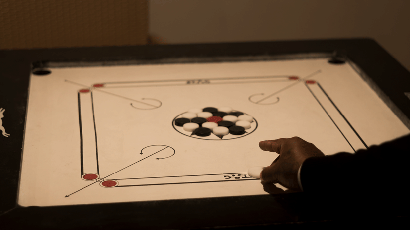 A close-up shot of a hand skillfully maneuvering a striker on a brightly lit carrom board during a game - Digantaa Resort in Mukteshwar