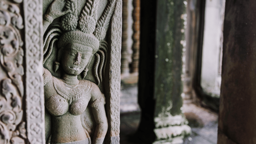 Ancient stone carving of a serene female figure with intricate details, possibly a deity or apsara, within a weathered temple structure