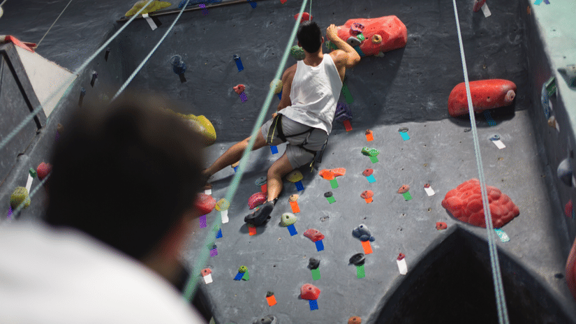 People indoor rock climbing on a colorful artificial wall with various holds, showcasing different skill levels and techniques