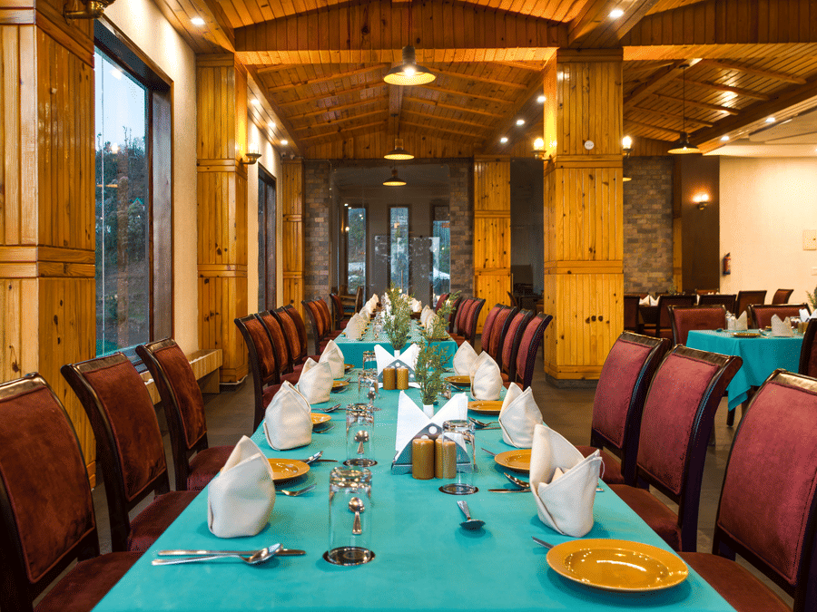 An elegantly set dining table in a spacious restaurant with warm lighting, ready for a delightful culinary experience with a scenic view - Digantaa Resort in Mukteshwar