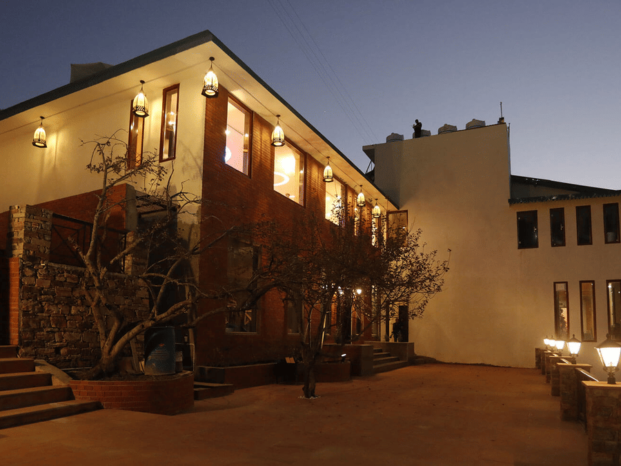 A grand building with warm lights illuminating its exterior at dusk, nestled on a hillside