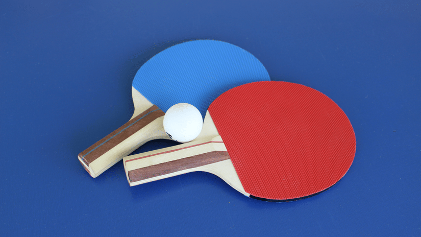 A pair of contrasting table tennis rackets with wooden handles are neatly arranged on a solid background, ready for a match