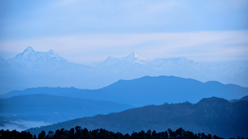 A serene landscape of layered blue mountain ranges under a clear, pale blue sky, depicting depth and tranquillity